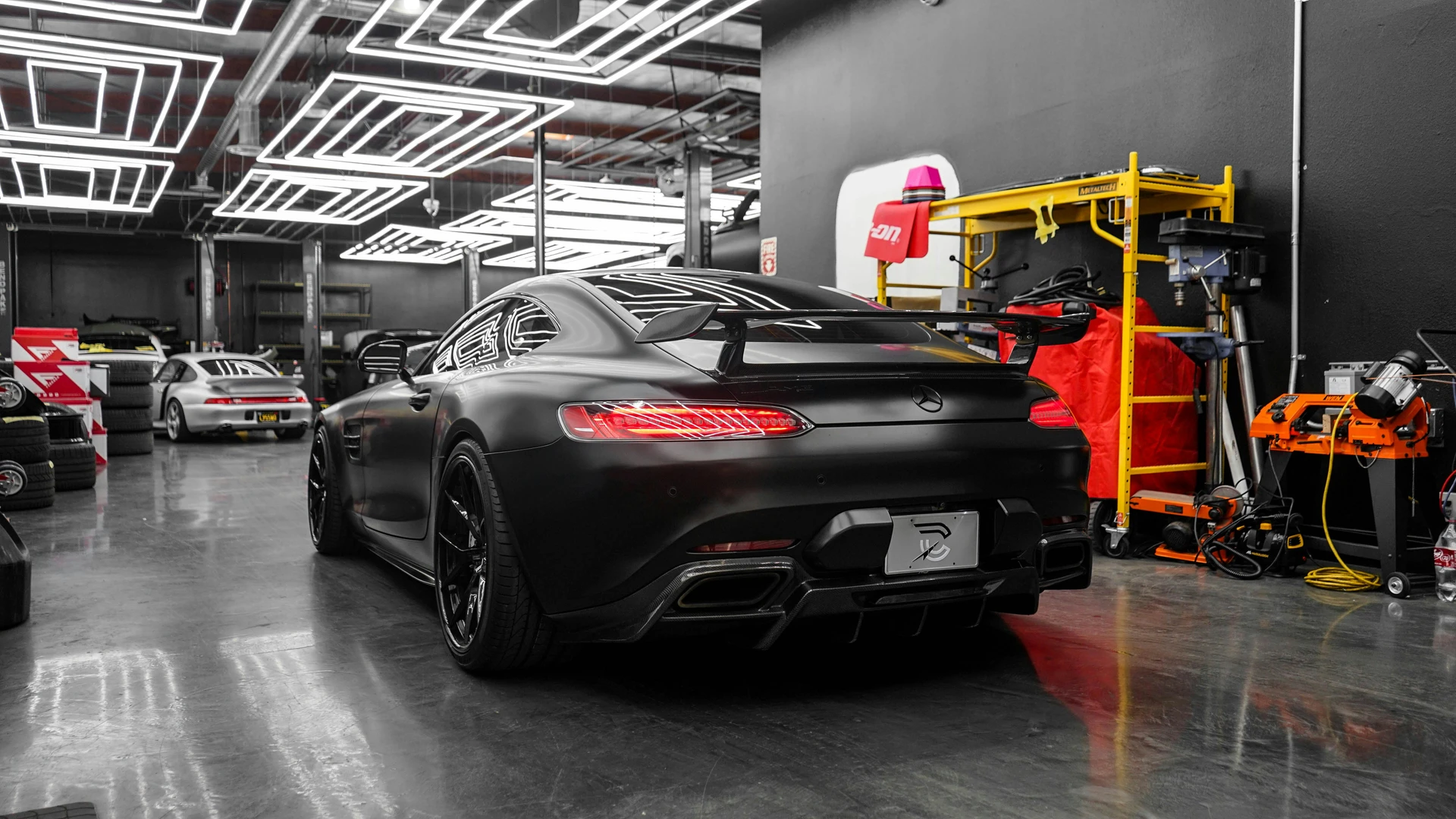 Mattschwarzer Mercedes-AMG GT von schräg hinten zwischen weiteren Fahrzeugen in der Halle
